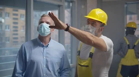 Male customer and foreman in protective mask examining renovation process Stock Photos