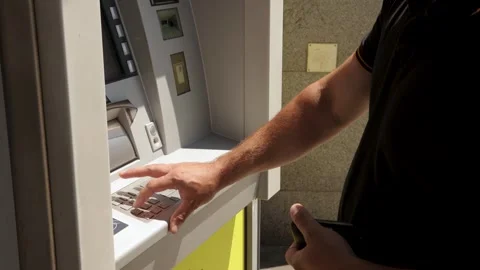 Male customer entering PIN code on ATM keypad outdoors, illustrating finance, Stock Footage 317512993