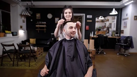 Male customer visiting barber shop and female barber. Man looking at himself in Stock Footage