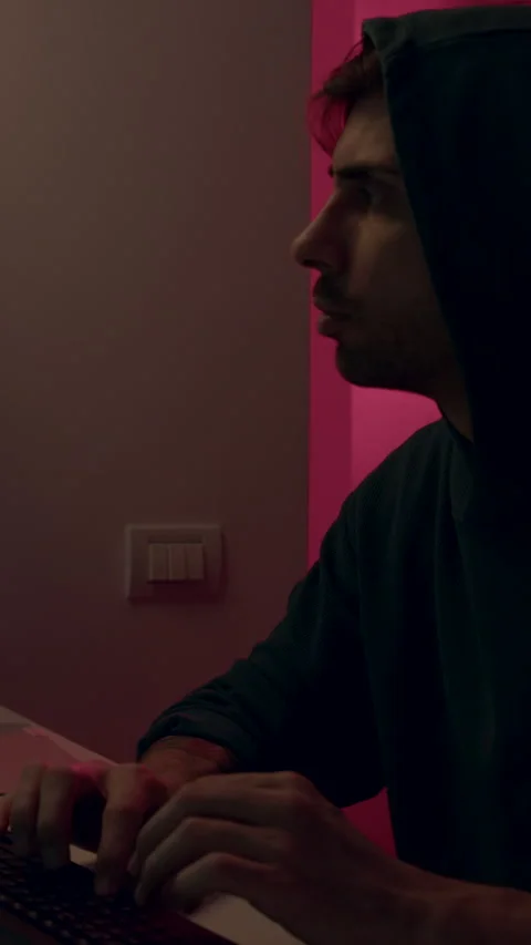 Male cyber security analyst in dark hoodie focused on computer screen, analyzing Stock Footage 323744014