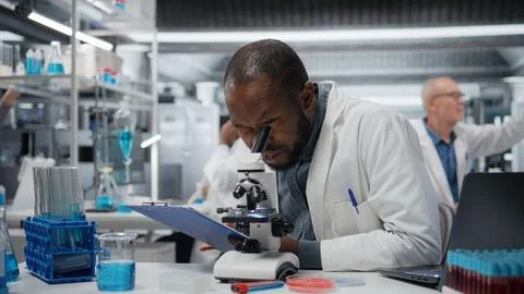 Male cytotechnologist using optical microscope to study microorganisms Stock Photos