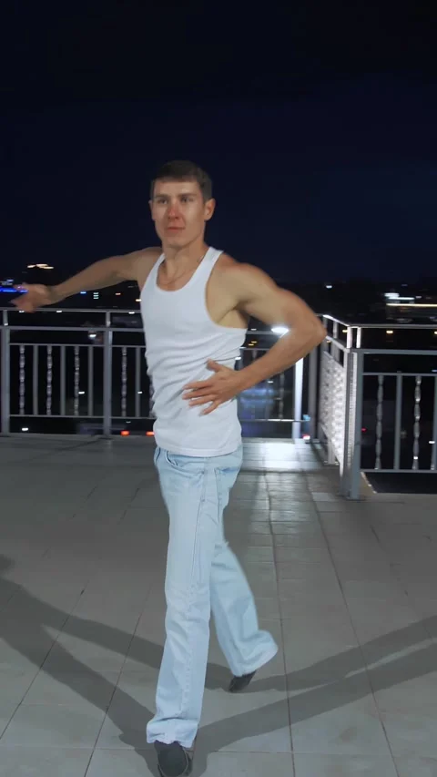 Male dancer performing dynamic movements on rooftop at night with city lights in Stock-Footage 313259740