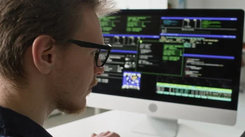 Male Developer in Glasses Reviewing Code on Computer Screens in IT Office Stock Footage 330123983