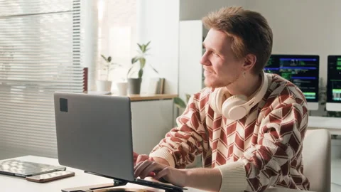 Male Developer with Headphones Looking at Sunlight while Using Laptop in Office Stock Footage 330132890