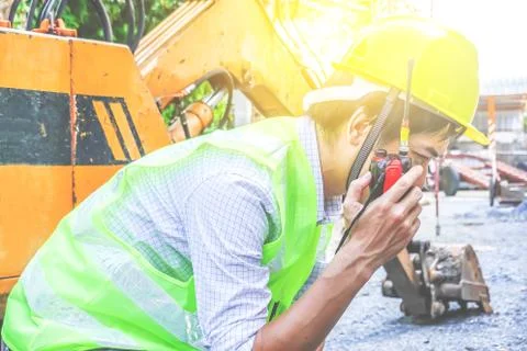 Male developer sitting and talking on the walkie talkie with an excavator Stock Photos