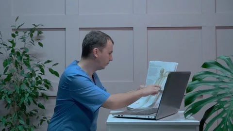 Male doctor conducting a study using laptop and reference materials. Video stock 121301328