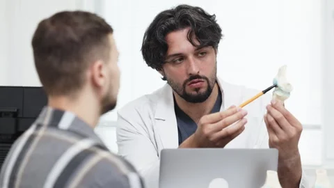 Male doctor explaining knee joint anatomy to a male patient using a model while Stock Footage 339980312
