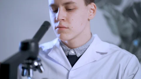 Male doctor looking through a microscope observing viruses, recording observa Stock-Footage 128244525