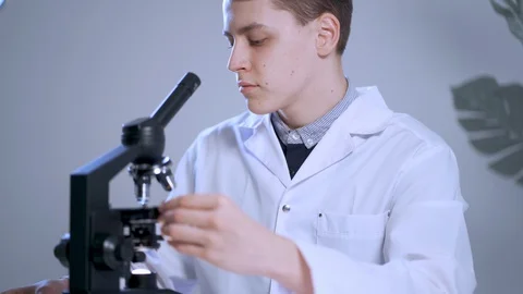 Male doctor looking through a microscope observing viruses, recording observa Stock Footage 128244705