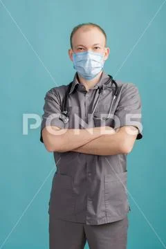Male doctor in mask with stethoscope looking at camera on blue background Stock Photos