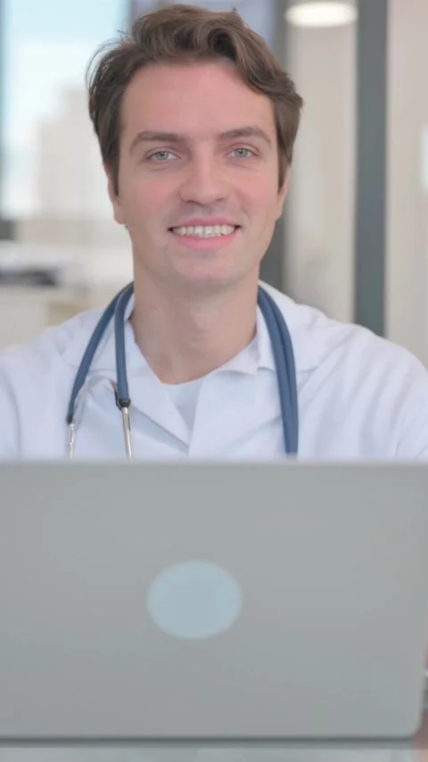 Male Doctor Smiling at Camera while Working on Laptop, vertical video Video stock 324793069