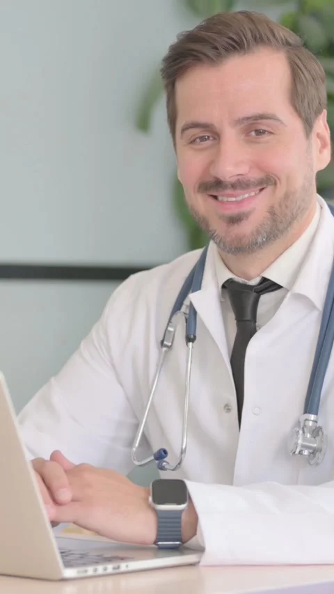 Male Doctor Smiling at Camera while Working on Laptop, vertical video Video stock 328557305