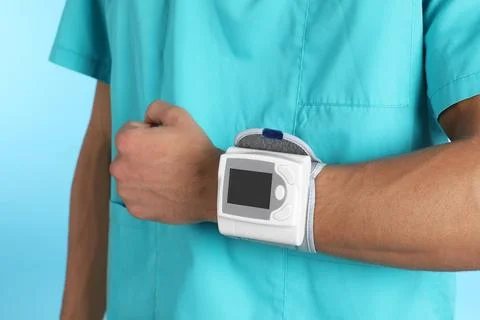 Male doctor using blood pressure monitor on color background, closeup. Medica Stock Photos
