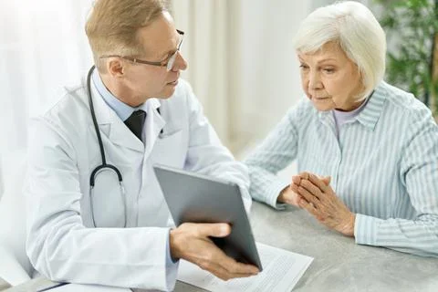 Male doctor using tablet computer while talking with old woman Stock Photos