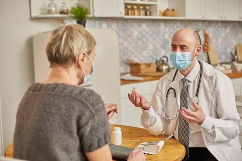 A male doctor wearing a protective mask advises an elderly woman wearing a Stock Photos