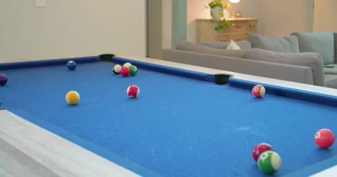 Male with dreadlocks lining up and striking shot at home on blue-felt pool table Stock Footage 340257016