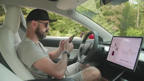 Male driver uses a smartphone, while Tesla Autopilot drives his vehicle Stock Footage 236959125
