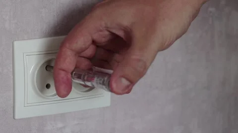A male electrician checks the current in the socket with a screwdriver with an Stock Footage 246736881