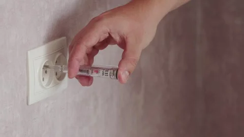 A male electrician checks the current in the socket with a screwdriver with an Stock Footage 249651136