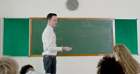 Male elementary teacher invites answer time near chalkboard as young girl walks Stock Footage 341930885