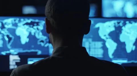 Male employee monitors maps and data on computer display screens in dark office Stock Footage