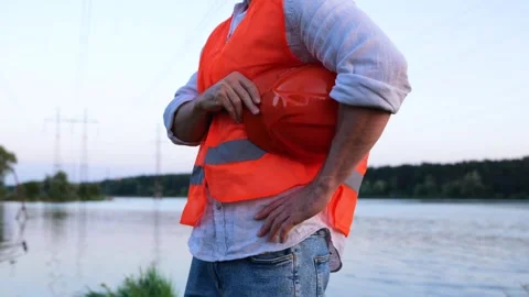 Male engineer holding helmet, posing outdoors with beautiful river on the Stock Footage 252267852