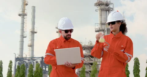 Male engineer points toward refinery unit while female technician holds flask, Stock Footage 334828712
