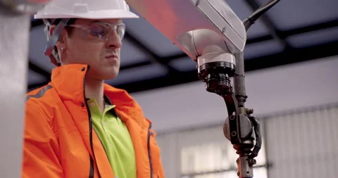 Male engineer in protective glasses and helmet tests robotic welding system 库存影片 313649546