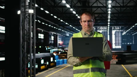 Male engineer supervises workshop fabrication equipment and checking laptop Stock Footage 321915361