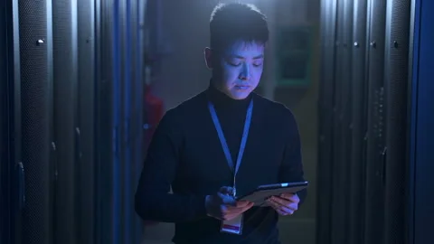 Male engineer using device and checking equipment racks while walking in data Stock Footage 162224258