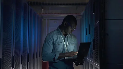 Male engineer using laptop and examining equipment while standing in dark server Stock Footage 161744357