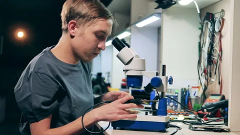 Male engineer is using a microscope to fix a microcircuit Stock Footage 145540667