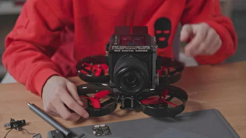Male engineer working on drone, using camera. Close-up of young man in red Stock Footage 186158060