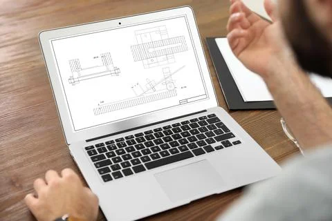 Male engineer working with technical drawing on laptop indoors, closeup Foto stock