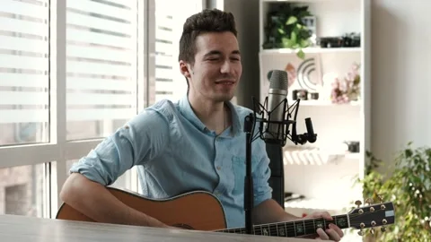 Male enjoy singing and playing Guitar while sitting on sofa at home Stock Footage 202276216