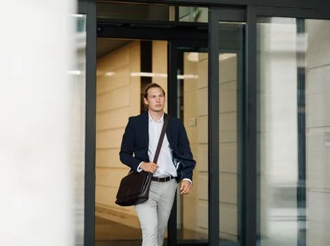 Male entrepreneur exiting from office building through automatic doors Stock Photos
