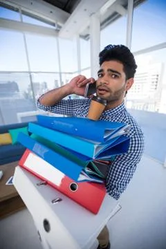 Male executive holding stack of files while talking on mobile phone Foto stock