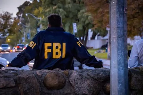 Male FBI agent wearing dark blue coat with FBI logo looking down the street with Stock Photos