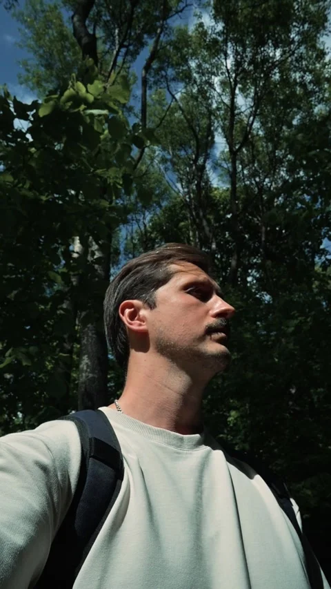 A male figure looks up while walking through a wooded area filled with trees and 動画素材 344440273