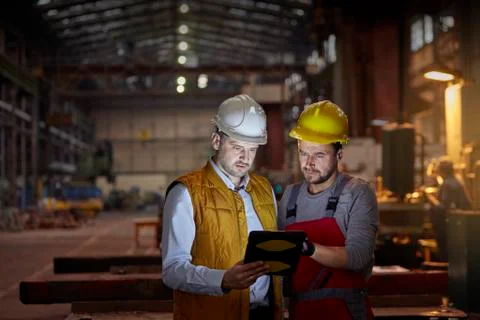 Male foreman and engineer using digital tablet in dark factory Stock Photos
