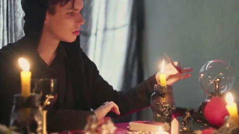 Male fortune teller looking at a magic taro card and moving it over a candle Video stock 143512064
