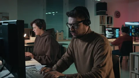 Male Fraudster Typing on Computer while Talking to Victim at Scam Call Center Stock Footage 310269706