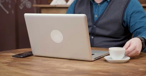 Male freelancer sips coffee while working from a small coffee shop. Stock Footage 105399555