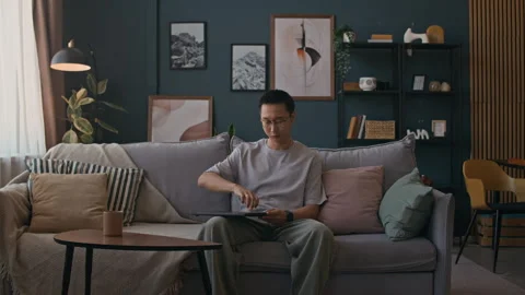 Male Freelancer Sitting down on Sofa Working on Laptop in Living Room Stock Footage 316296921