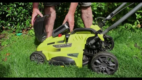 Male Gardener inserting a Lithium Ion battery on a electric cordless lawnmowe Stock Footage 343874656