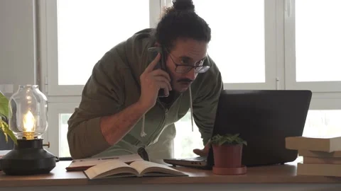 Male getting angrier on phone while checking laptop Stock Footage 162107342