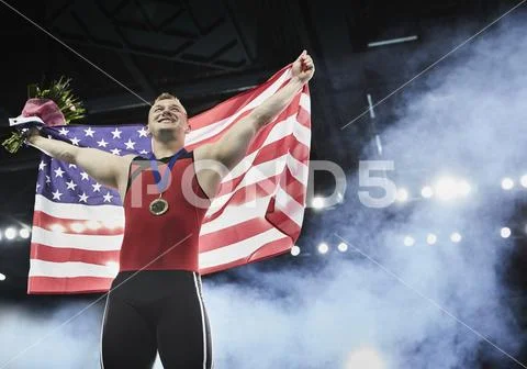 Male gymnast celebrating victory holding American flag on winners podium Stock Photos