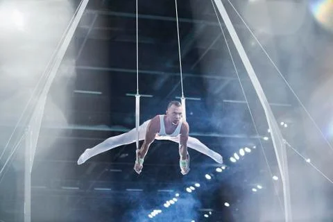 Male gymnast performing on gymnastics rings in arena Stock Photos