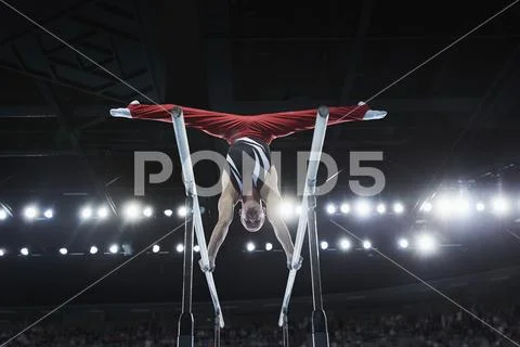 Male Gymnast Performing Upside-Down Splits On Parallel Bars In Arena