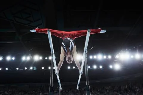 Male gymnast performing upside-down splits on parallel bars in arena Stock Photos